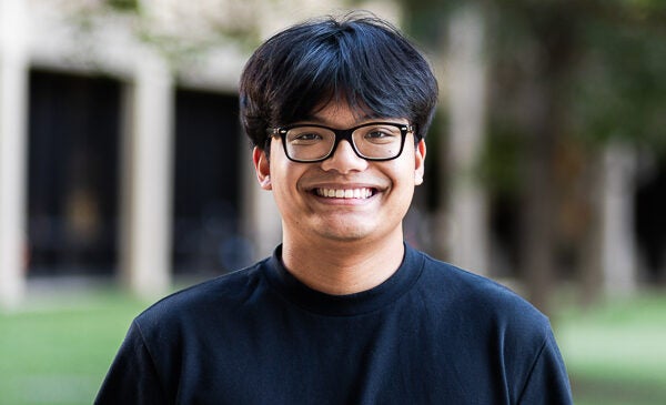 Student smiles while wearing black glasses and black t shirt