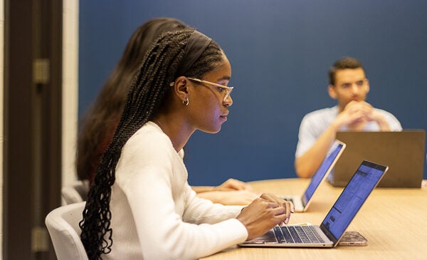 Student leans over desk to write on laptop computer