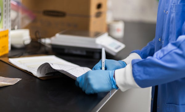 Student writing on paper in lab with blue medical gloves on