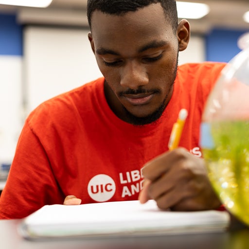 Student wearing red UIC t shirt writes in notebook